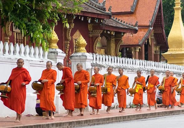 Monks walking through ancient temple grounds in Luang Prabang at sunrise.